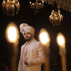 A regal groom's portrait. The warm glow of the lights and the grand chandeliers in the background complement his elegant sherwani and poised stance.