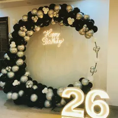 A chic and modern 26th birthday celebration. This C-shaped balloon arch in black and silver is paired with a "Happy Birthday" neon sign and large light-up numbers.