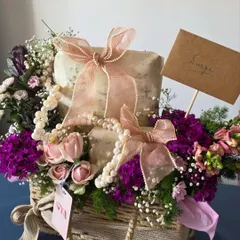 This wicker basket arrangement showcases a classic approach to trousseau gifting. Gifts are wrapped in textured paper and tied with pearl-studded ribbons, surrounded by a mix of fresh pink and purple flowers.