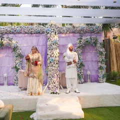 The couple on their Nikah stage, set against a beautiful lavender backdrop with white and blue floral arches. The open-air setting adds a touch of natural serenity.
