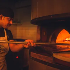 The heart of our kitchen. Our pizzaiolo carefully tends to a pie in the wood-fired oven, where temperatures get hot enough to cook a Neapolitan pizza in just 60 to 90 seconds.