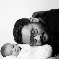 A father and his newborn share a quiet moment in this beautiful black and white portrait. The high-contrast lighting creates a simple yet powerful image.