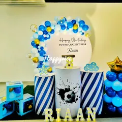 A football-themed birthday for Riaan. The decor features a blue, white, and gold balloon arch, striped pedestals, and a soccer ball graphic for a sporty celebration.