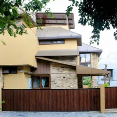 A full view of the home's facade, showing the interplay of different volumes, sloped roofs, and materials. The large wooden gate provides a warm and secure entrance.