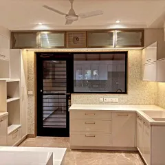 This view shows the kitchen's connection to the outdoors through a large window and door. The layout includes overhead cabinets above the window for extra storage.