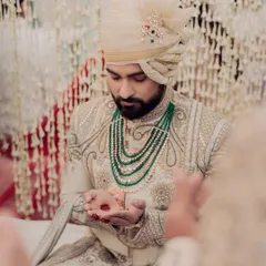 The groom, Bismil, during the Nikah rituals. His attire, with its intricate embroidery and emerald green necklace, perfectly complements the pastel green and white decor palette.