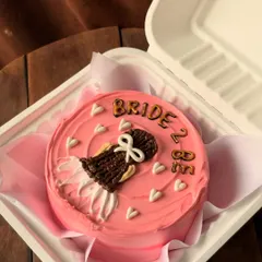 A perfect cake for a bridal shower or to celebrate a bride-to-be. This pretty pink bento cake is decorated with a drawing of a wedding dress and the words "Bride 2 Be," surrounded by tiny white hearts.