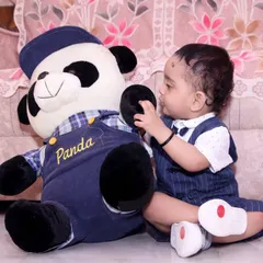 An indoor baby portrait session where the baby is interacting with a large teddy bear prop.