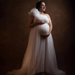 A classic and elegant solo portrait from a studio session. The soft lighting and the beautiful white one-shoulder gown create a timeless, angelic look that focuses on the joy of the mother-to-be.