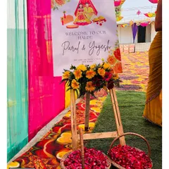 A beautiful welcome easel for a Haldi ceremony, featuring custom graphics of a bride and groom, along with baskets of fresh petals for the guests.