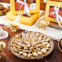 A close-up of dog-friendly 'kaju katli', specially made for pets. The elegant styling with diyas and festive boxes makes it look like a true Diwali delicacy.