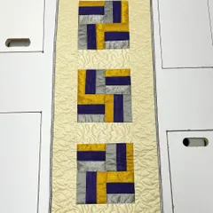 An elegant table runner crafted from shimmering silk fabric in shades of gold, purple, and silver. The luxurious material and intricate quilting make it perfect for special occasions.