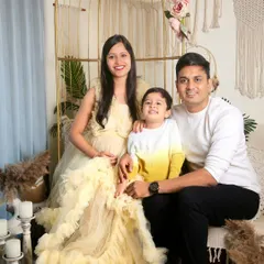 A classic family portrait with the mom-to-be seated, surrounded by her husband and son. Everyone is smiling for the camera in our cozy, boho-themed studio.