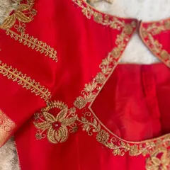 The neckline detail of a custom red blouse. The intricate floral vine pattern is created with precise Aari embroidery, a key skill we teach in our Indian embroidery module.