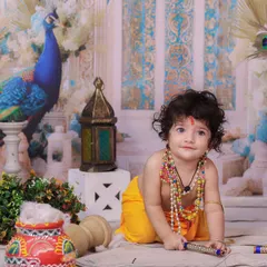 A sweet and innocent portrait of a baby dressed as Krishna, crawling on the floor amidst festive props. The soft lighting highlights his curly hair and gentle expression.