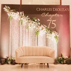 This elegant photo booth backdrop was designed for a 75th birthday party. It features a custom "Chapter 75" sign, a cascade of shimmering crystals, and beautiful floral arrangements, providing a perfect spot for memorable pictures.