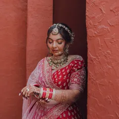 A classic bridal portrait, with the bride adjusting her bangles. This shot highlights her intricate jewelry and the rich color of her lehenga.