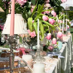 A detailed view of the tablescape for the Bridgerton luncheon. The decor includes pink tulips, vintage lampshades, classic candlesticks, and strings of pearls, creating a lavish and romantic feel.