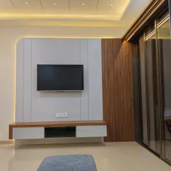 A minimalist TV unit design with a clean white paneled backdrop and a contrasting vertical wood panel. The floating console below offers concealed storage, maintaining a sleek and uncluttered look.
