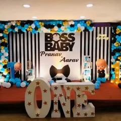 A stylish Boss Baby theme for a first birthday celebration. The stage features a black and white striped backdrop, character cutouts, and large 'ONE' marquee letters.