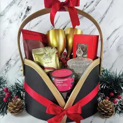 A holiday hamper designed for celebration. This basket features golden goblets, cocktail mix, and cranberry treats, all tied together with a festive red ribbon against a classic marble background.