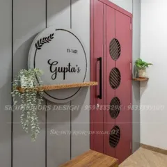 A modern and personalized entrance with a large circular nameplate and a sleek red door. The floating shelf with a trailing plant adds a touch of nature.