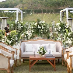 A sophisticated lounge area for the garden reception, featuring classic furniture, custom monogrammed cushions, and lush arrangements of white flowers and greenery.