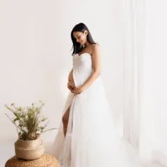 So angelic and serene. This mom-to-be chose a simple, elegant white tulle gown from my collection for her studio session. The soft lighting from the window creates a gentle glow, perfect for a peaceful solo maternity portrait.