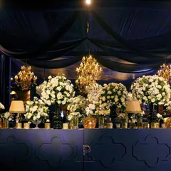 The bar was a focal point, featuring a mirrored front with a quatrefoil pattern and a backdrop of deep blue. It was topped with massive urns of white florals and golden lamps, reflecting the grandeur of the evening.
