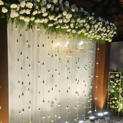 A close-up of the engagement backdrop, highlighting the delicate hanging jasmine buds and the lush white rose arrangement. The uplighting creates a warm and romantic glow.