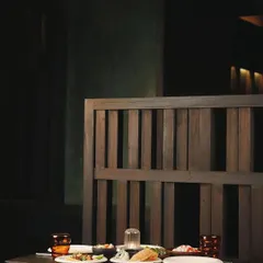 A table set for two at Otra. The dark wood of the furniture and partitions, combined with the soft, focused lighting, creates an intimate and sophisticated dining environment.