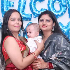 A photo of two women holding a newborn baby at a celebration with 'Welcome Baby Boy' balloons. We document these happy gatherings for new parents.