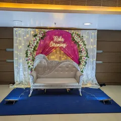 An elegant stage for a Roka ceremony at a banquet hall, designed with a floral ring, white and pink drapes, fairy lights, and a custom 'Roka Ceremony' neon sign.