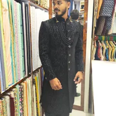 The power of a black sherwani is unmatched. This piece is crafted from a self-patterned jacquard fabric and styled with a matching beaded necklace for a sleek, modern, and elegant groom's look.
