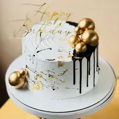 A chic white cake with black drips and gold spheres, a modern and stylish choice for any birthday.