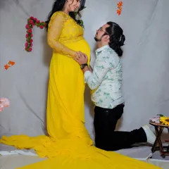 A classic studio pose filled with adoration. The partner kneels to connect with the baby bump, while the vibrant yellow gown adds a splash of joy and brightness to this pregnancy portrait.