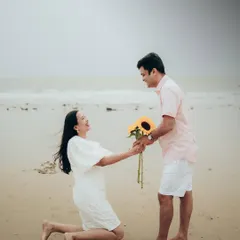 A playful and romantic proposal moment on the sand, with sunflowers adding a bright, cheerful touch to this casual beach pre-wedding shoot.