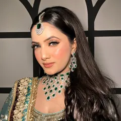 This angle highlights the beautiful emerald jewelry and how it complements the soft, peachy tones of the makeup.