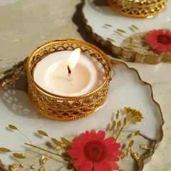 This is a close-up of my resin floral diya. The base is made of white resin with preserved red flowers and gold flakes, and it holds a golden filigree tea light holder.