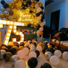 Celebrating a 75th birthday with a room full of joy. This home decoration features a balloon arch in black, gold, and white, large light-up marquee numbers, and dozens of balloons scattered on the floor for a festive feel.