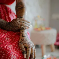 A detail-oriented shot focusing on the bride's hands, covered in elaborate mehndi. Her red outfit provides a beautiful contrast to the dark henna.