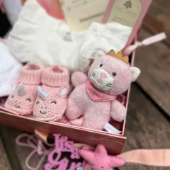 Inside a celestial-themed hamper for a baby girl, you'll find unicorn booties, a soft onesie, and a crowned kitty plush toy, all nestled in a beautiful keepsake box.
