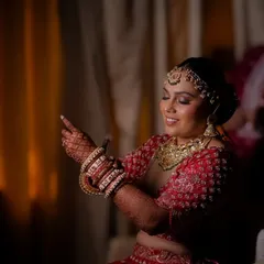 A candid moment during the bridal getting-ready process, the bride smiles as she adjusts her bangles, the warm lighting creating an intimate feel.