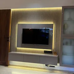 A well-designed TV unit can be the centerpiece of a living room. This floating unit features a laminate finish, a fluted panel wall with concealed backlighting, and a glass-fronted display cabinet for a clean and sophisticated entertainment area.