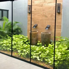 Bringing the calmness of water indoors. This modern courtyard features twin minimalist wall spouts cascading into rustic urns, surrounded by lush greenery. A floor-to-ceiling glass wall seamlessly integrates this piece of peace into the home's interior living space.