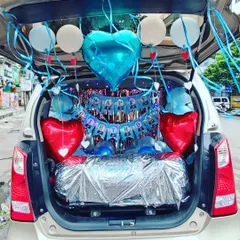 A birthday car trunk setup with a blue and red theme. This decoration includes heart-shaped foil balloons, a 'Happy Birthday' banner, and a wrapped gift, all ready for the big surprise.