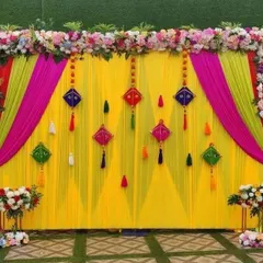 A bright and colorful backdrop perfect for a Haldi or Mehndi ceremony. This setup features a yellow curtain with pink and green drapes, decorated with traditional kite hangings.