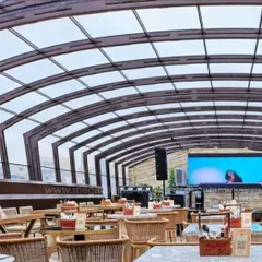 An arched retractable roof installed at a commercial venue. This solution allows the business to operate in any weather, providing a clear view of the sky on good days and full protection during rain.