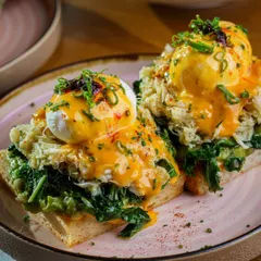 A luxurious take on Eggs Benedict, topped with crab meat and a vibrant hollandaise sauce. The close up shot highlights the rich textures and premium ingredients, perfect for an upscale brunch menu.
