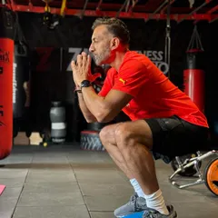 A senior client working on his balance and leg strength by performing squats on stability pods. These exercises are crucial for improving stability and preventing falls.